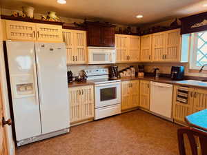 Kitchen featuring sink, white appliances, light tile patterned floors, and decorative backsplash