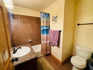 Full bathroom with a textured ceiling, toilet, tile patterned floors, shower / bathtub combination with curtain, and vanity