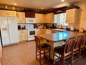 Kitchen featuring white appliances, a kitchen bar, kitchen peninsula, and light tile patterned floors