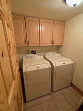 Washroom with cabinets, a textured ceiling, light tile patterned floors, and washer and clothes dryer