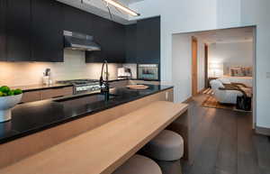 Kitchen with wall chimney range hood, dark hardwood / wood-style floors, oven, and a breakfast bar