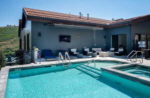 View of pool-hot tub with an outdoor living space, television and retractable awning. Adjacent to community room and outdoor grill