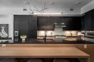 Kitchen with range, a breakfast bar, stainless steel oven, wall chimney exhaust hood, and sink