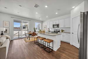 Kitchen with dark hardwood / wood-style flooring, an island with sink, a breakfast bar, white cabinets, and appliances with stainless steel finishes