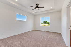 Carpeted empty room with ceiling fan and a raised ceiling