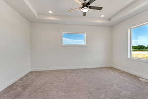 Carpeted empty room featuring a tray ceiling and ceiling fan