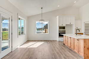 Kitchen featuring lofted ceiling, light hardwood / wood-style flooring, stainless steel oven, white cabinets, and sink