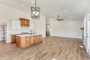 Kitchen featuring white cabinetry, light hardwood / wood-style flooring, ceiling fan with notable chandelier, an island with sink, and high vaulted ceiling