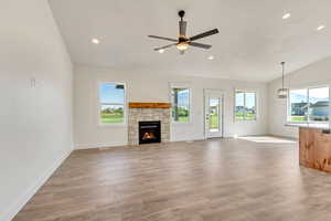 Unfurnished living room featuring a stone fireplace, lofted ceiling, light wood-type flooring, and ceiling fan