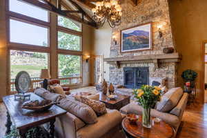 Living room with beam ceiling, a stone fireplace, wood-type flooring, and high vaulted ceiling