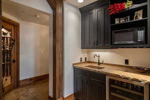 Bar with sink, dark brown cabinetry, light stone countertops, light tile patterned flooring, and wine cooler