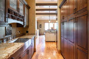 Kitchen with crown molding, light stone counters, light hardwood / wood-style floors, beamed ceiling, and pendant lighting