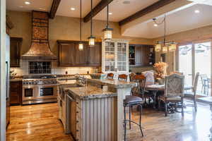 Kitchen featuring appliances with stainless steel finishes, pendant lighting, premium range hood, a kitchen island with sink, and light wood-type flooring