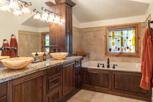 Bathroom featuring double sink vanity, a tub to relax in, a notable chandelier, and plenty of natural light