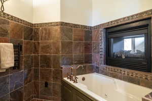 Bathroom featuring tiled bath, radiator heating unit, and tile walls