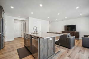 Kitchen with a kitchen island with sink, appliances with stainless steel finishes, light stone countertops, light wood-type flooring, and sink