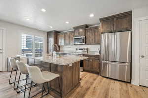 Kitchen featuring an island with sink, stainless steel appliances, light hardwood / wood-style flooring, and light stone countertops