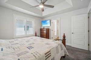 Bedroom featuring dark carpet, connected bathroom, a tray ceiling, and ceiling fan