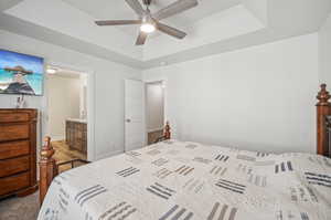 Bedroom with ensuite bath, carpet, ceiling fan, and a raised ceiling