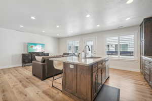 Kitchen featuring light hardwood / wood-style flooring, a kitchen island with sink, light stone countertops, a kitchen breakfast bar, and sink