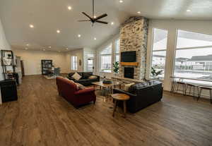 Living room featuring a stone fireplace, dark wood-type flooring, high vaulted ceiling, and ceiling fan