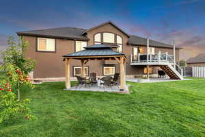 Back house at dusk featuring a deck, a lawn, a patio area, and a gazebo