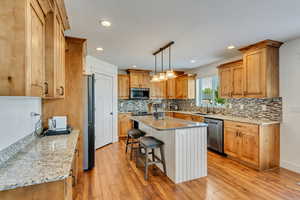 Kitchen featuring stainless steel appliances, sink, light stone counters, hanging light fixtures, and light hardwood / wood-style floors