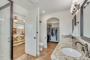 Bathroom with tile patterned floors, double sink vanity, toilet, and ceiling fan