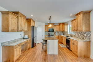 Kitchen featuring a breakfast bar area, light hardwood / wood-style flooring, stainless steel appliances, decorative light fixtures, and a center island