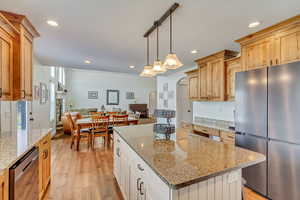 Kitchen with light wood-type flooring, light brown cabinets, light stone countertops, a kitchen island, and appliances with stainless steel finishes