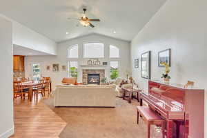 Living room featuring a fireplace, light colored carpet, high vaulted ceiling, and ceiling fan