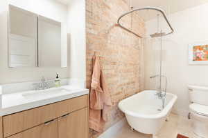 Full bathroom with brick wall, modern vanity, toilet, bathtub/shower combination, and light tile floors