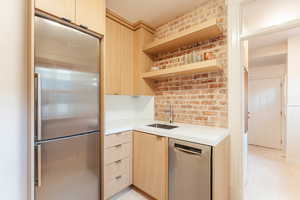 Kitchen featuring light brown modern cabinetry, stainless steel appliances, brick wall, and sink