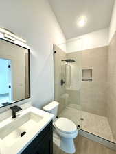 Bathroom with vanity, a tile shower, wood-type flooring, and toilet