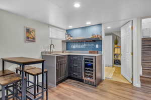 Bar with dark brown cabinetry, wine cooler, sink, and light hardwood / wood-style floors