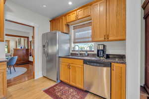 Kitchen featuring light hardwood / wood-style flooring, sink, stainless steel appliances, and dark stone countertops