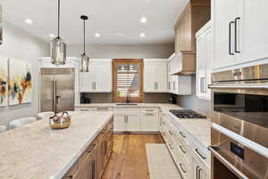 Kitchen with appliances with stainless steel finishes, white cabinets, light wood-type flooring, and tasteful backsplash