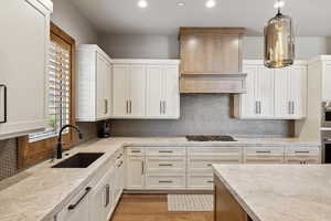 Kitchen featuring tasteful backsplash, light hardwood / wood-style floors, white cabinets, sink, and decorative light fixtures