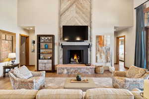 Living room featuring a stone fireplace, light hardwood / wood-style floors, and a towering ceiling