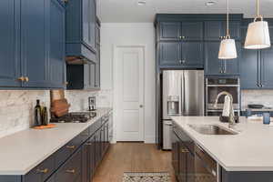 Kitchen featuring appliances with stainless steel finishes, wood-type flooring, decorative backsplash, and hanging light fixtures