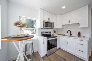 Kitchen with white cabinets, stainless steel appliances, sink, and light hardwood / wood-style floors