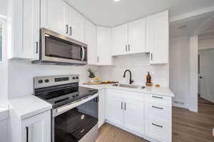 Kitchen with light wood-type flooring, decorative backsplash, stainless steel appliances, white cabinets, and sink