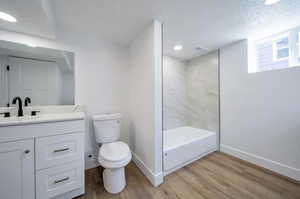 Full bathroom featuring a textured ceiling, toilet, vanity, tiled shower / bath, and wood-type flooring