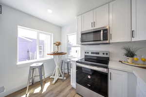 Kitchen featuring tasteful backsplash, stainless steel appliances, light hardwood / wood-style flooring, and white cabinets