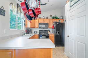 Kitchen featuring black appliances, sink, kitchen peninsula, lofted ceiling, and light tile patterned flooring