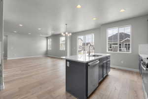 Kitchen featuring a textured ceiling, light wood-type flooring, sink, a kitchen island with sink, and stainless steel dishwasher