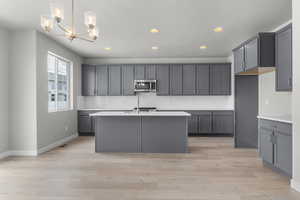 Kitchen with gray cabinets, light hardwood / wood-style flooring, an inviting chandelier, hanging light fixtures, and a center island with sink