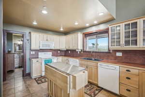 Kitchen with sink, light brown cabinetry, white appliances, and light tile patterned floors