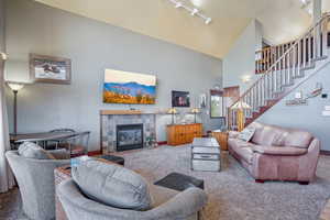 Carpeted living room featuring a tile fireplace, track lighting, and a high ceiling