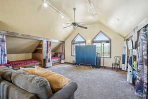 Carpeted living room featuring ceiling fan, lofted ceiling, and rail lighting